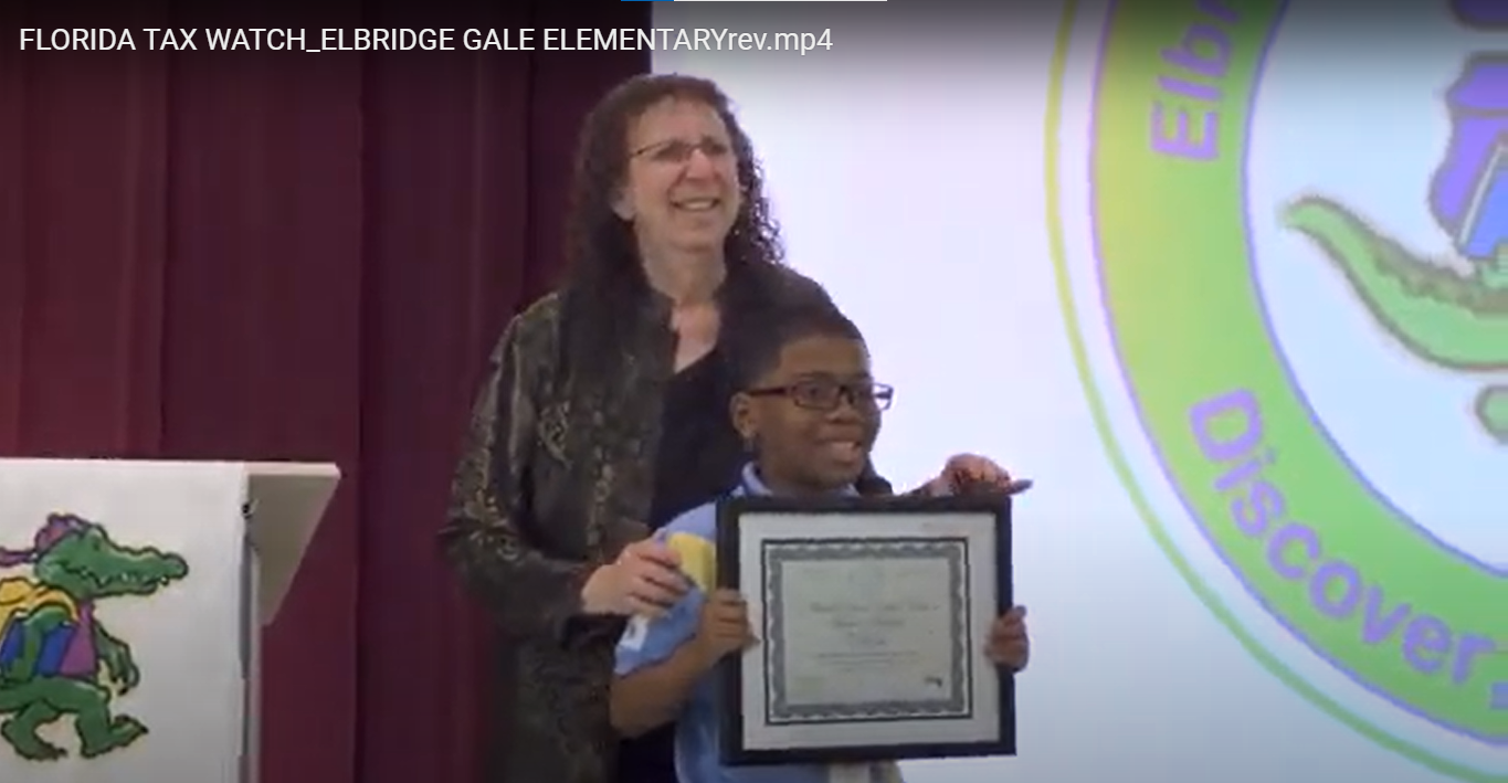  Elbridge Gale principal Gail Pasterczyk standing behind a male student on stage, holding an award